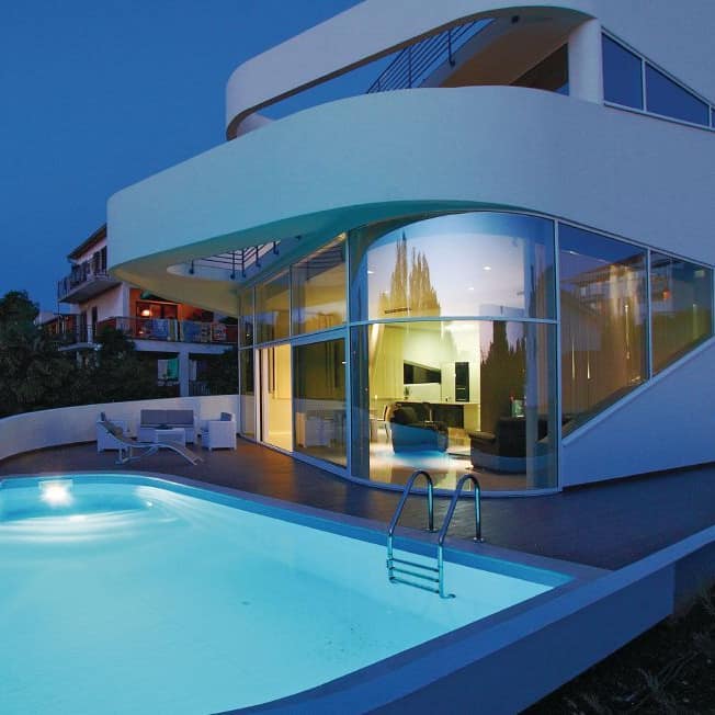 Modernes Ferienhaus auf Krk mit großer Fensterfront und beleuchtetem Pool in der Abendstimmung