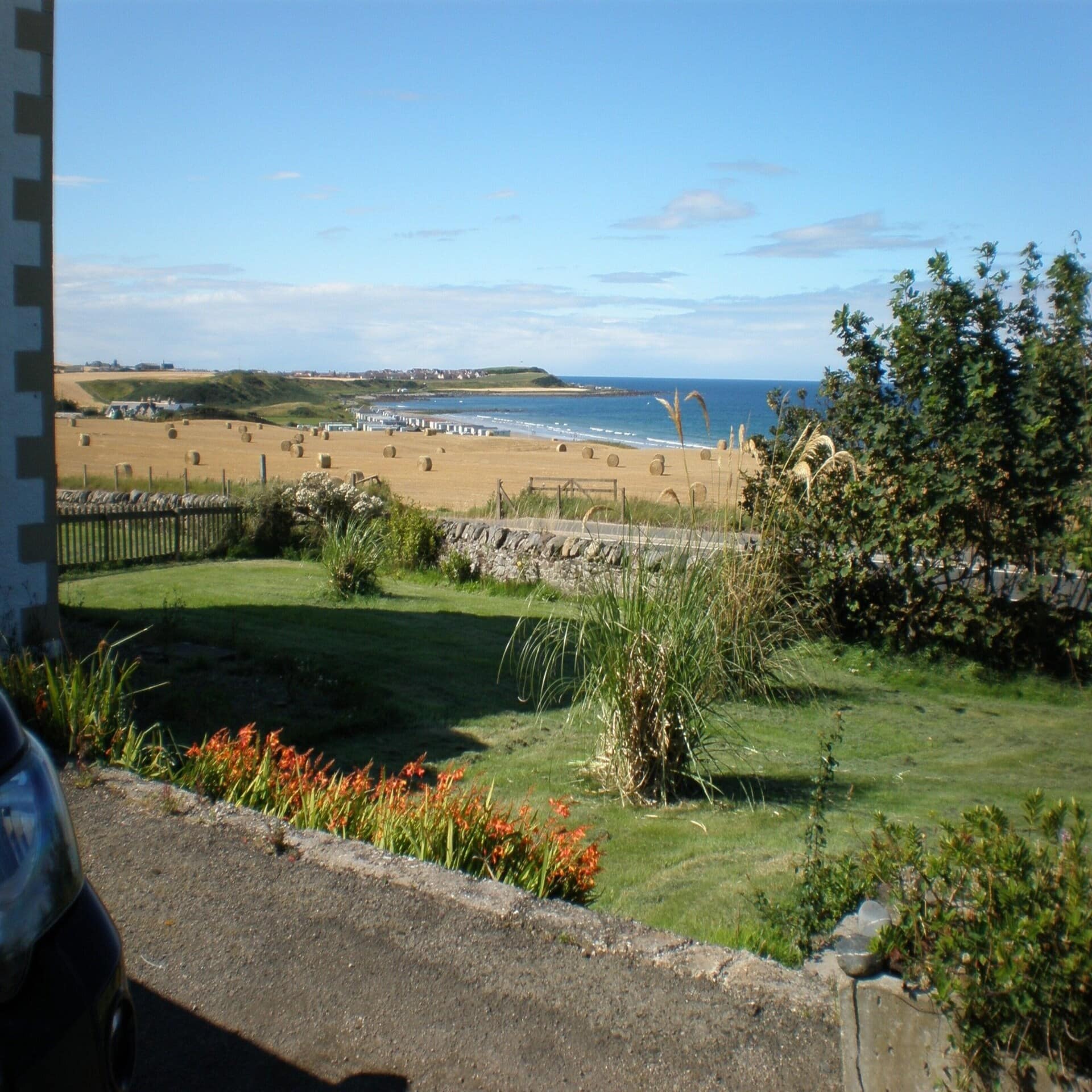 Garten eines Bauernhauses mit Blick über die Felder mit Strohballen und die Nordsee in Schottland. 