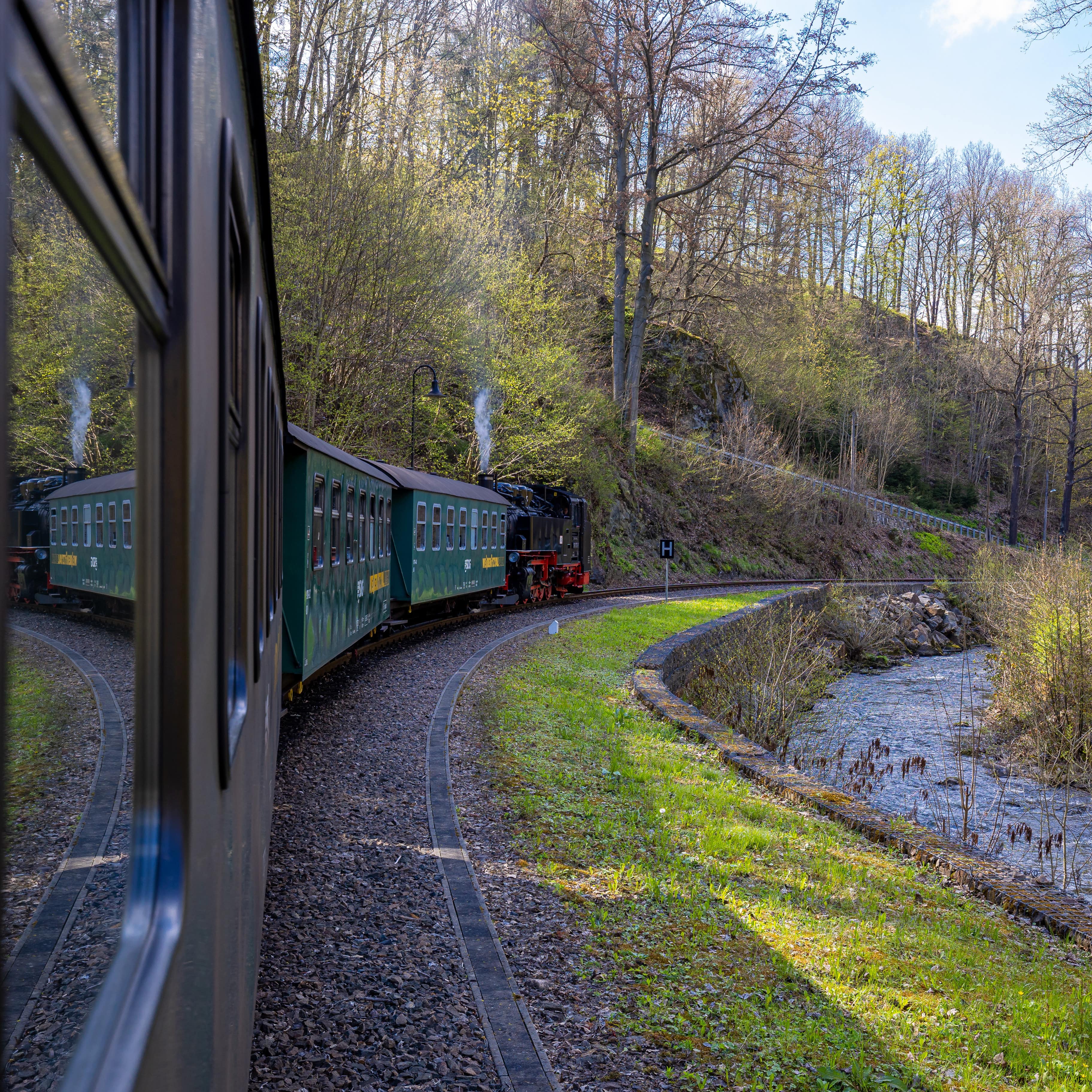 Blick aus einem Wagon der Weißeritztalbahn am Zug entlang, vorne die Lok, rechts ein Bach.